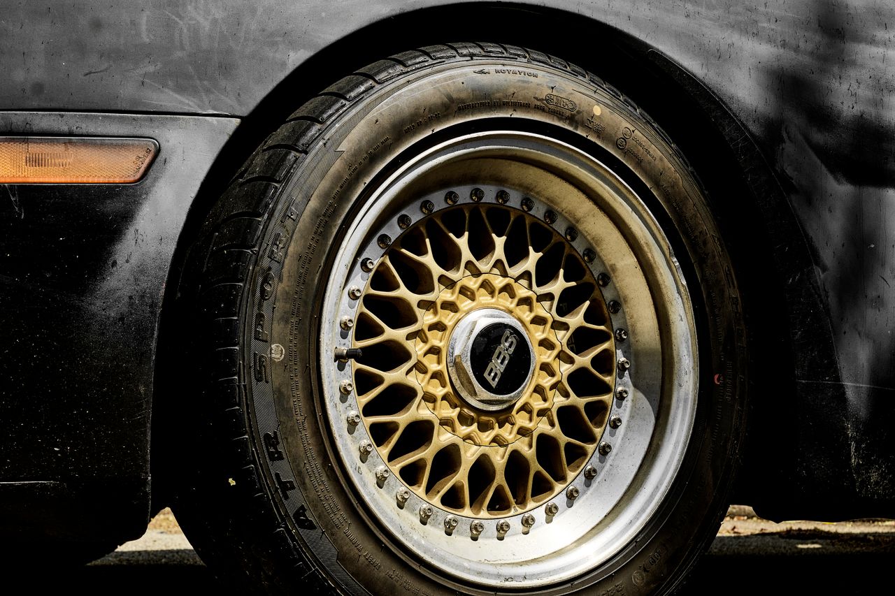 Detailed view of a black car's wheel showcasing intricate gold rim design.