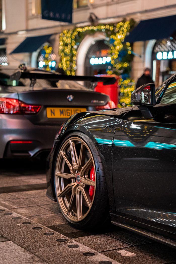 Sleek sports cars parked on a London street at night with festive lights in the background.