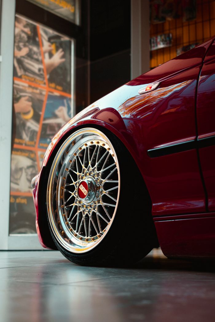 Detailed view of a custom red sports car wheel, showcasing intricate alloy design indoors.